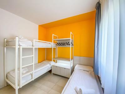 Zimmer mit zwei Etagenbetten und einem Einzelbett vor orangefarbener Wand und Vorhang.
