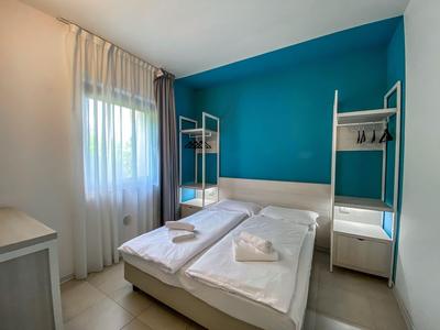 Helles Hotelzimmer mit zwei Einzelbetten, türkisfarbener Wand und Gardinen.