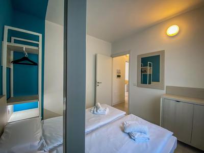 Modernes, helles Hotelzimmer mit Doppelbett, offenem Kleiderständer und minimalistischem Design.