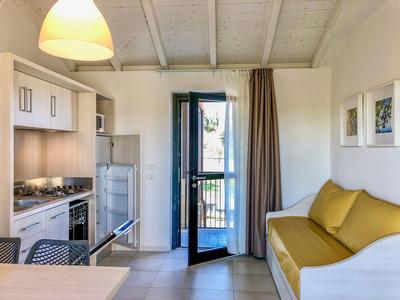 Kleine Küche und gelbes Sofa in hellem, modernem Ferienzimmer mit Zugang zum Balkon.