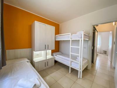 Schlicht eingerichtetes Hotelzimmer mit Etagenbett und Einzelbett, orangefarbener Wand.