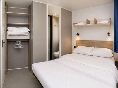 Modernes Hotelzimmer mit weißem Bett, offenem Schrank und minimaler Dekoration.