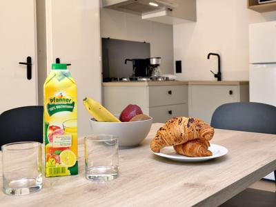 Küche mit Holztisch, Croissants, Obst und Saftkarton, modernes Ambiente.