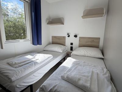 Zwei Einzelbetten mit weißen Bettlaken in einem schlichten, hellen Hotelzimmer mit Fenster.