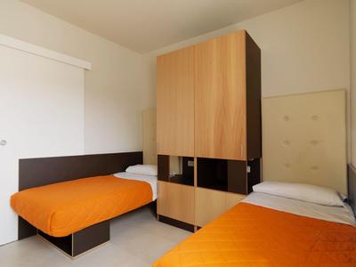 Ein Zimmer mit zwei Einzelbetten, orangenen Decken und einem braunen Schrank in der Mitte.