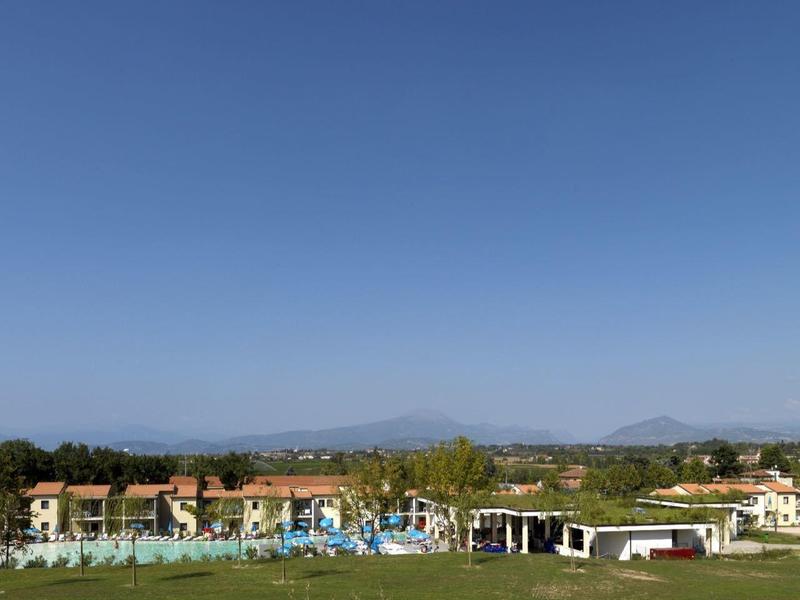 Reihenhäuser und Wiesen unter klarem, blauem Himmel mit Bergen am Horizont.