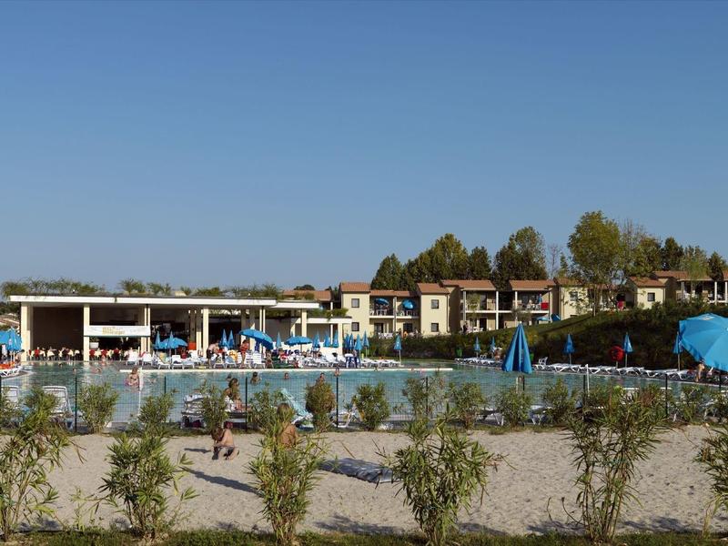 Großer Schwimmbadbereich mit Liegestühlen, Sonnenschirmen und mehreren Gebäuden im Hintergrund.
