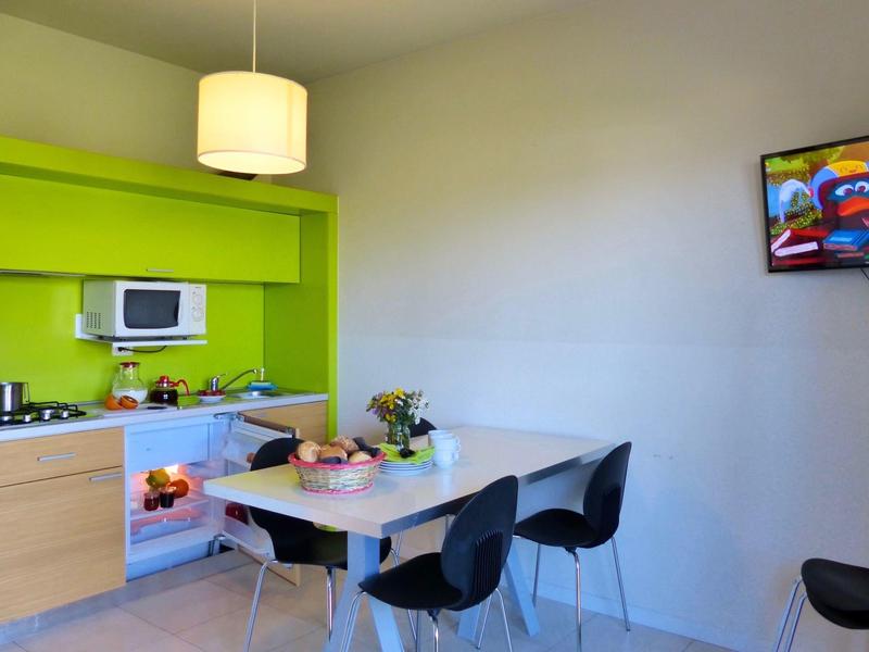 Moderne Küche mit grünen Schränken, weißem Tisch, schwarzen Stühlen und Wand-TV.