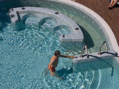 Dziecko wchodzi do okrągłego basenu z wbudowanym jacuzzi i drewnianym tarasem.