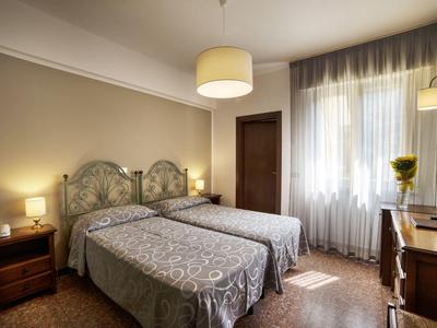 Jasny pokój hotelowy z dwoma pojedynczymi łóżkami, stolikiem nocnym, lampką i zasłonami przy oknie.