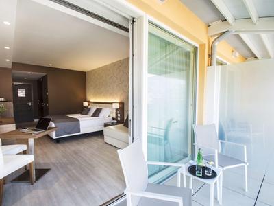 Nowoczesny balkon hotelowy ze szkła i białych krzeseł, widok na pokój z łóżkiem