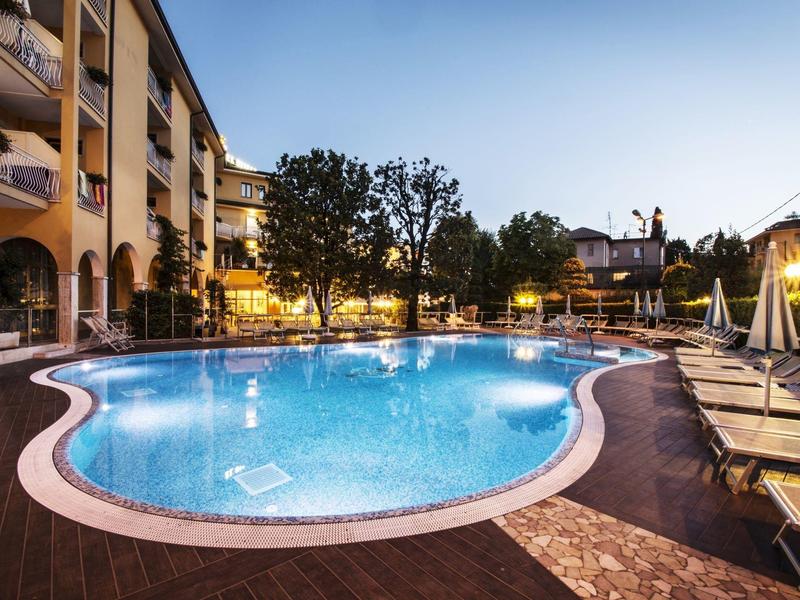 Oświetlony basen na zewnątrz z leżakami obok budynku hotelowego o zmierzchu.