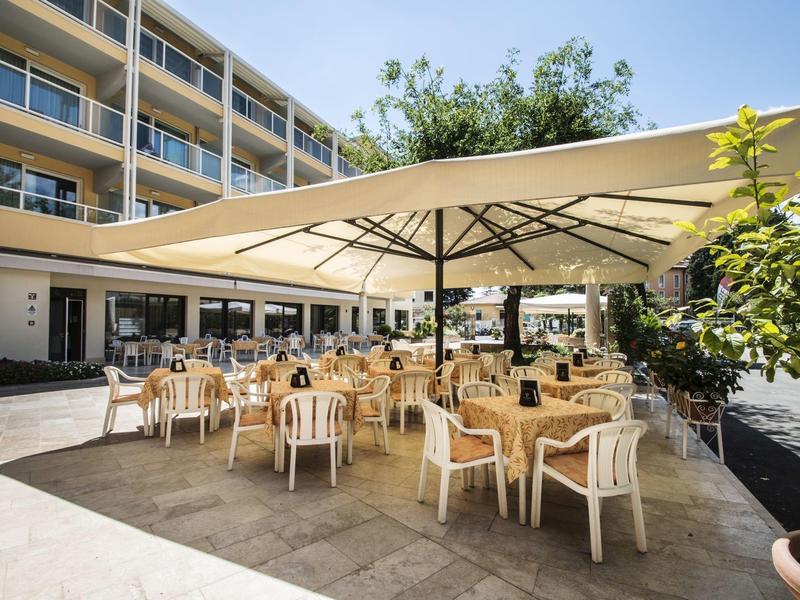 Teren hotelowy z nakrytymi stołami i dużym parasolem przeciwsłonecznym.