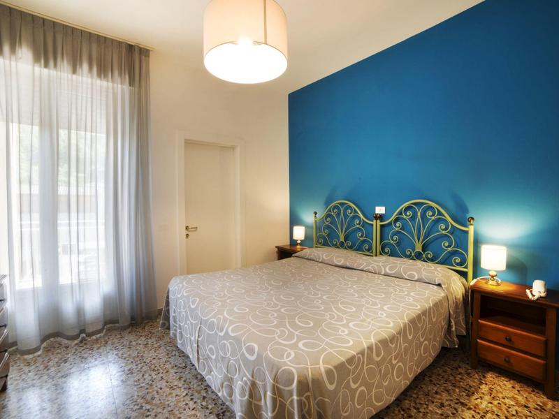 Jasno oświetlona sypialnia z łóżkiem podwójnym, niebieską ścianą akcentową i stolikami nocnymi.