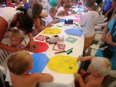Children paint colorful kites on paper at a long table during a group activity.