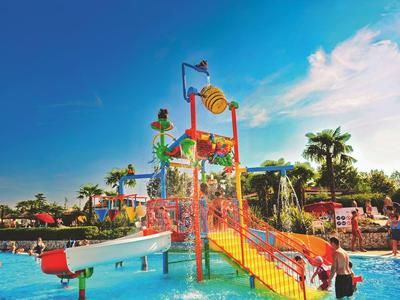 Colorful water playground with slide and fountains in a pool under a blue sky.