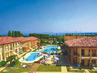 Hotelový komplex se dvěma budovami, dvěma bazény a lehátky pod modrou oblohou