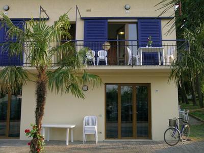 Balcony with blue railing, white chairs, and plants in front of a light-colored building.