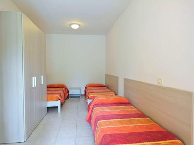 A simple hotel room with three single beds and a wardrobe on white tiled floor.