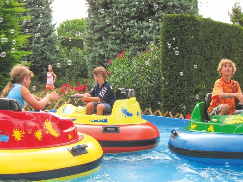 Several people smiling and sitting in colorful bumper boats on a water pool.