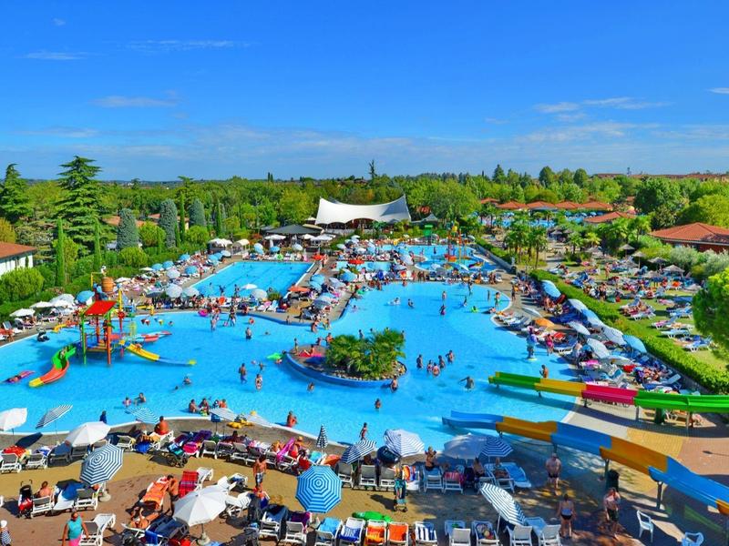 Large outdoor pool complex with water slides, sun loungers, and people on a sunny day