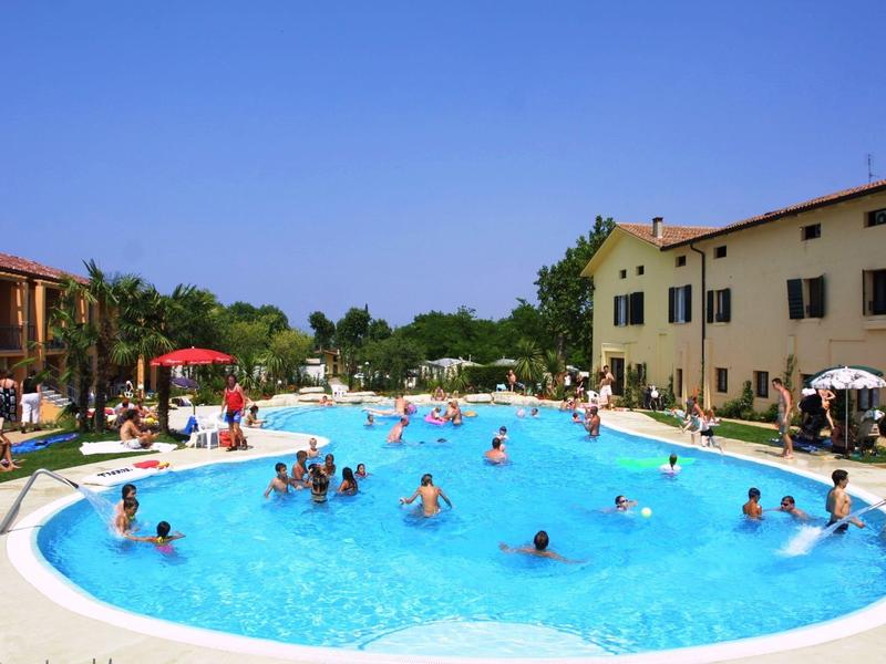 Large pool with many people between two hotel buildings under a blue sky