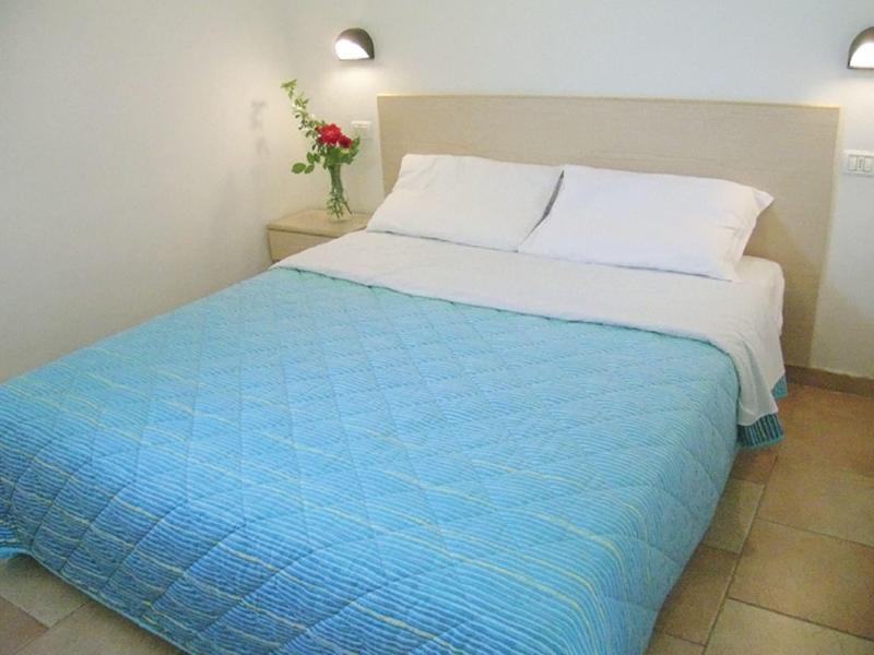 Simple hotel room with bed, blue quilt, and nightstand with flowers.