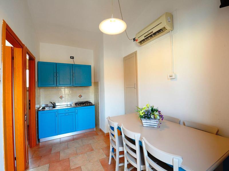 Small kitchen with blue cabinets, dining table with white chairs, and wall-mounted air conditioner.