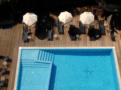 Vogelperspektive eines Pools mit Holzterrasse, Liegestühlen und weißen Sonnenschirmen.