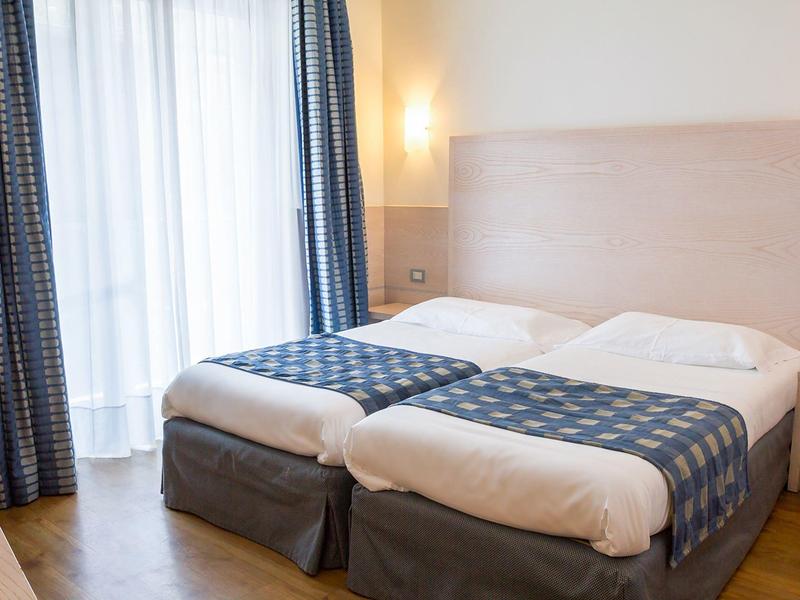 Camera d'hotel moderna con due letti singoli e grandi tende accanto alla finestra.