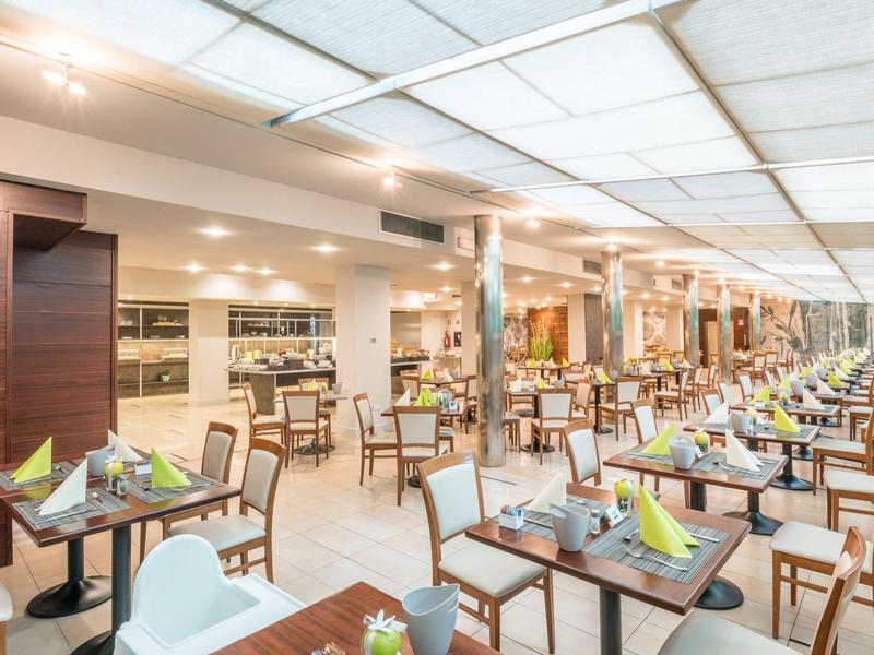 Ristorante luminoso e moderno con lunghe file di tavoli apparecchiati e sedie.