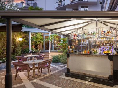 Beleuchtete Außenbar mit Stühlen und Tischen in einem Hotelgarten bei Dämmerung.