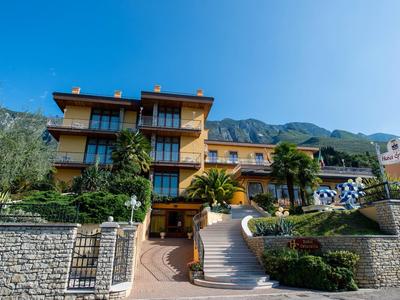 Hotel with stone wall and stairs, surrounded by greenery and mountains in the background.