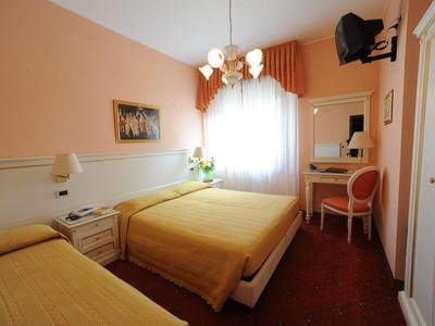 Brightly furnished hotel room with three beds, desk, and window with curtains.