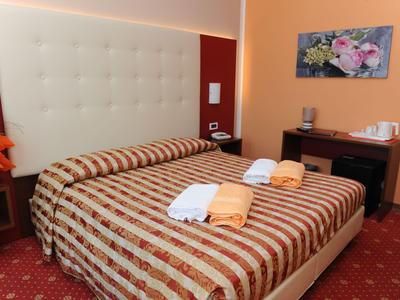 Hotelzimmer mit Doppelbett, gestreifter Tagesdecke und Handtüchern, Schreibtisch und Bild an der Wand.