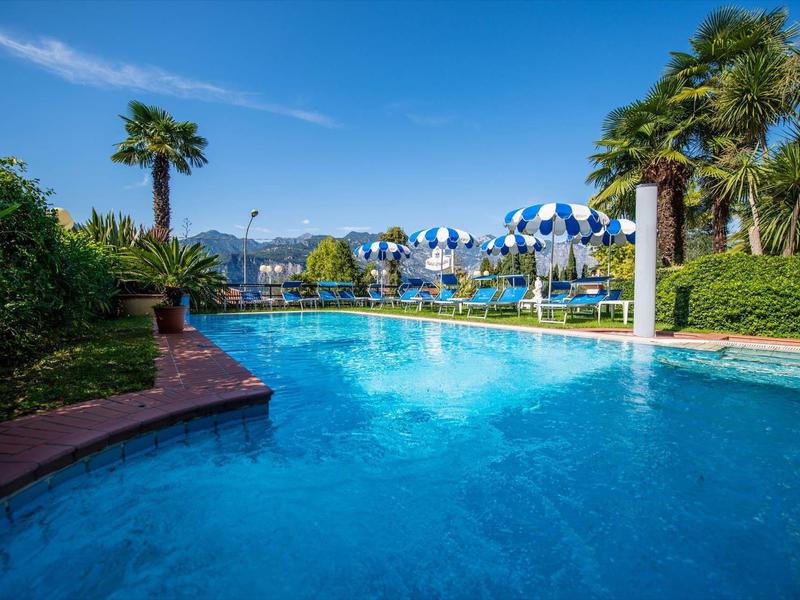 Outdoor pool with blue umbrellas and palm trees under clear sky.