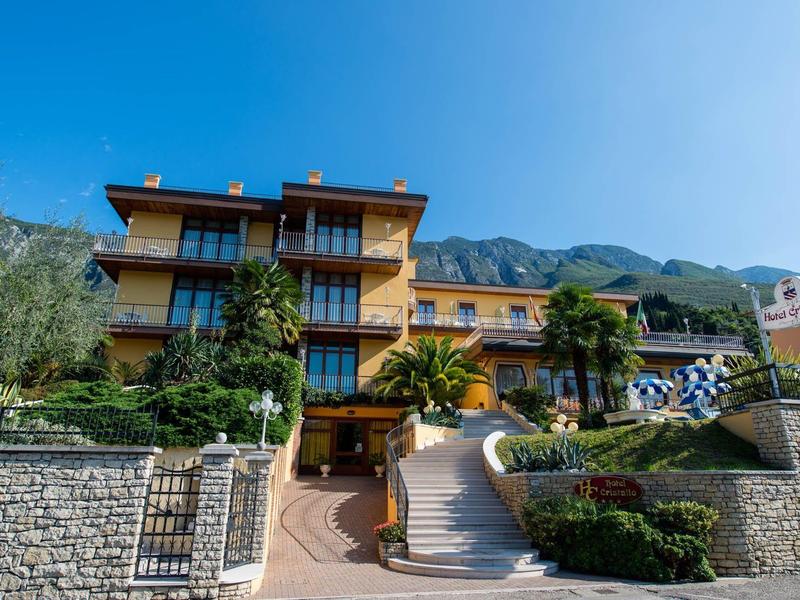 Hotel with stone wall and stairs, surrounded by greenery and mountains in the background.