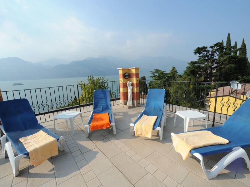 Rooftop terrace with blue loungers overlooking lake and mountains under clear sky.