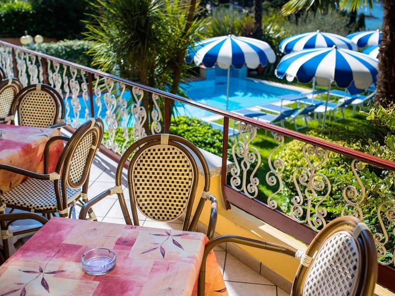 Balcony with set tables overlooking a pool with blue umbrellas.