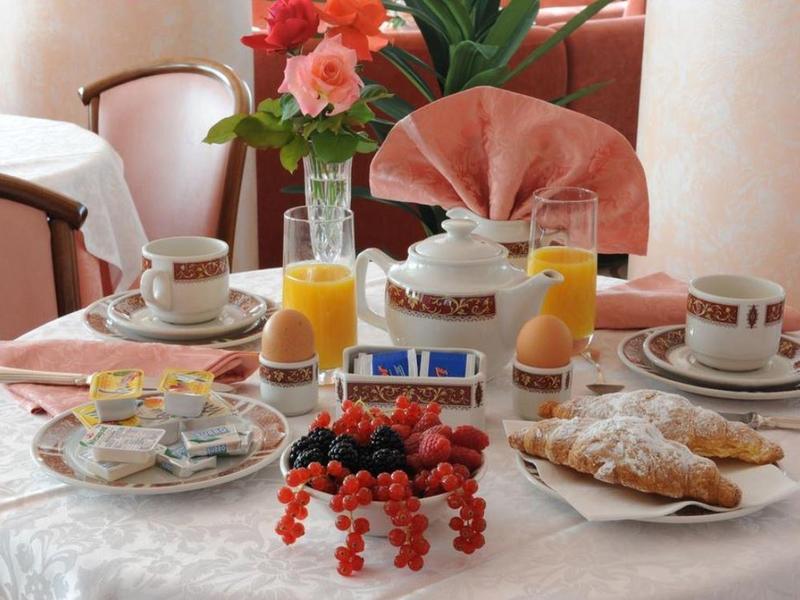 A breakfast table set with coffee, orange juice, pastries, and berries against pink walls.