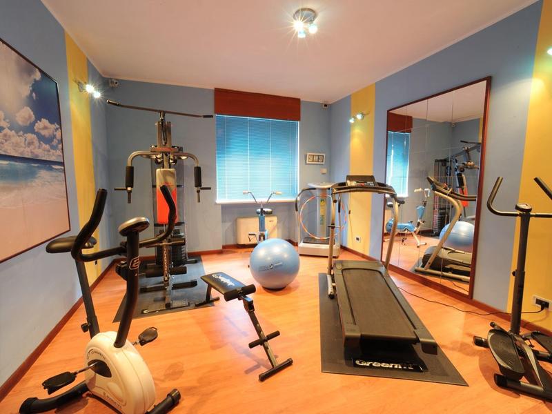 Small hotel gym with equipment, dumbbells, ball, and a wall mirror.