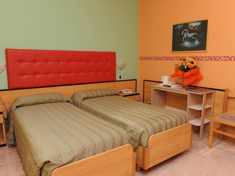 Hotel room with two single beds, red headboards, and a small table with flowers.