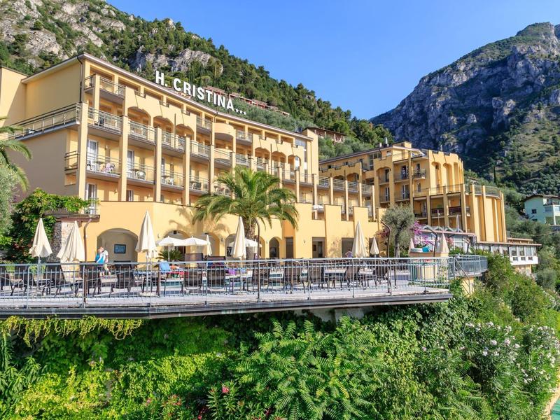 Edificio histórico de hotel con balcones y terraza exterior frente a paisaje montañoso y cielo azul.