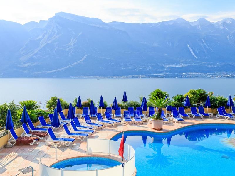 Área de piscina con tumbonas azules y sombrillas frente a lago montañoso en resort hotelero