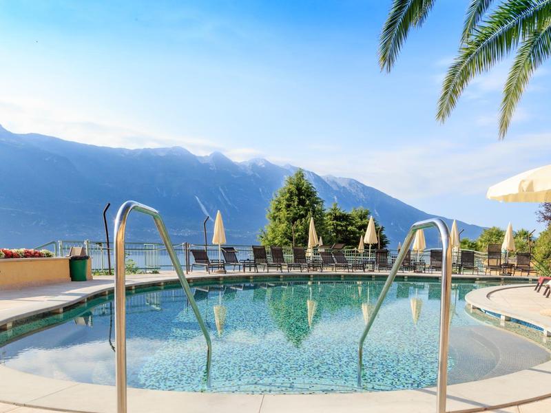 Piscina redonda con barandilla de metal, tumbonas y vista a las montañas bajo cielo despejado.