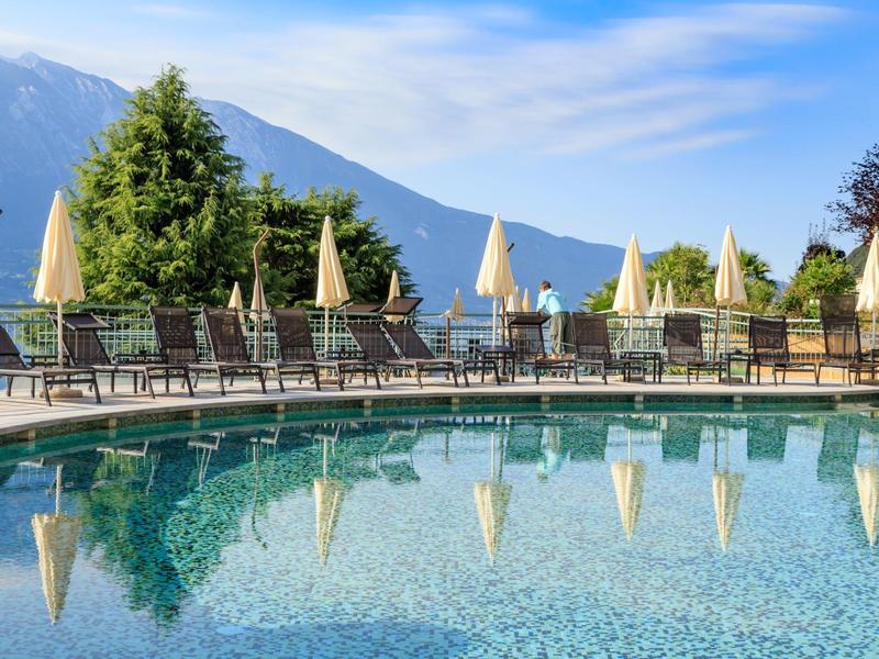 Piscina con tumbonas y sombrillas frente a montañas bajo cielo despejado.
