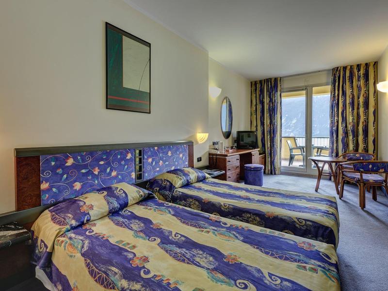 Habitación de hotel con dos camas individuales, edredones coloridos y ventana con vista exterior.