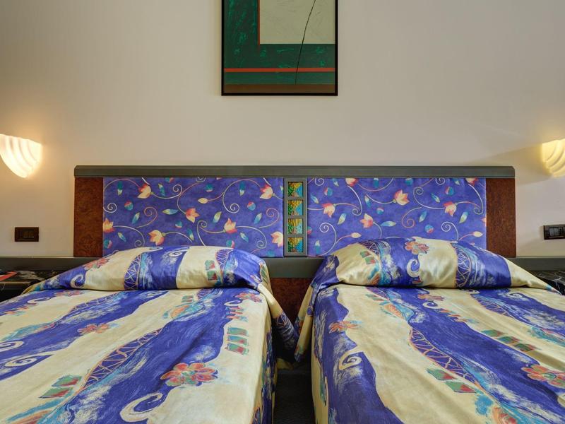 Dos camas individuales con colchas coloridas y una mesita de noche común entre ellas.