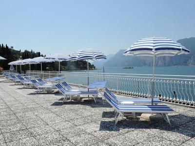 Liegestühle mit blauen und weißen Schirmen auf einer Terrasse mit Meerblick