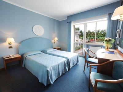 Camera d'hotel moderna con due letti, tonalità di blu e vista su un balcone.